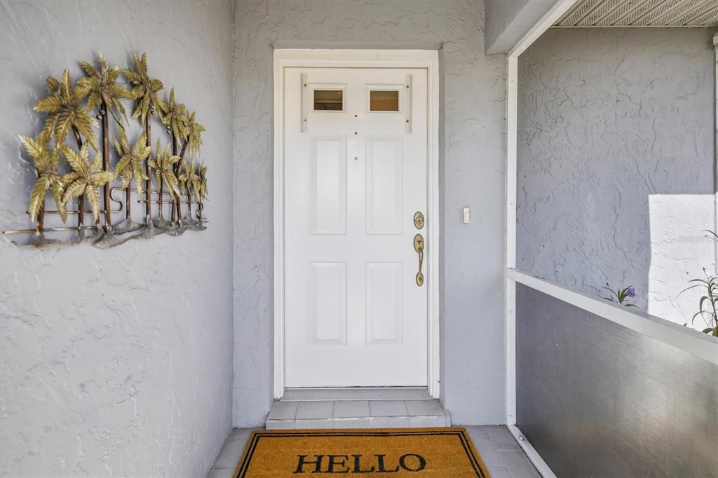 A white front door with a welcome mat sits in a covered entryway with gray walls — 26392 LANCER LANE, PUNTA GORDA, FL