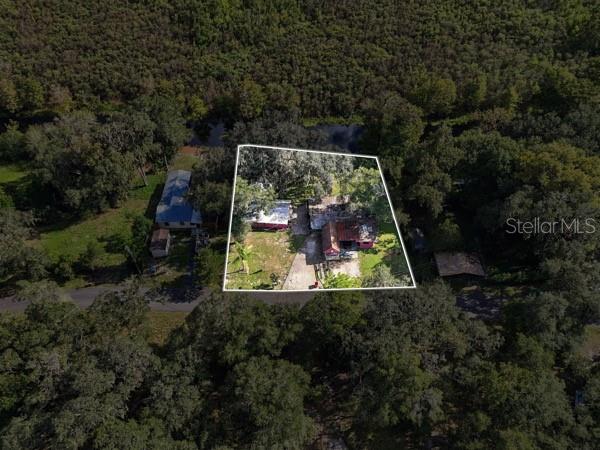 An aerial view shows a house with a metal roof situated on a wooded waterfront lot — 11717 E SALMON DRIVE, FLORAL CITY, FL