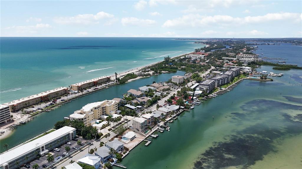 An aerial view shows a coastal community with multi-story buildings, boat docks, and sandy beaches — 9034 MIDNIGHT PASS ROAD UNIT 6, SARASOTA, FL