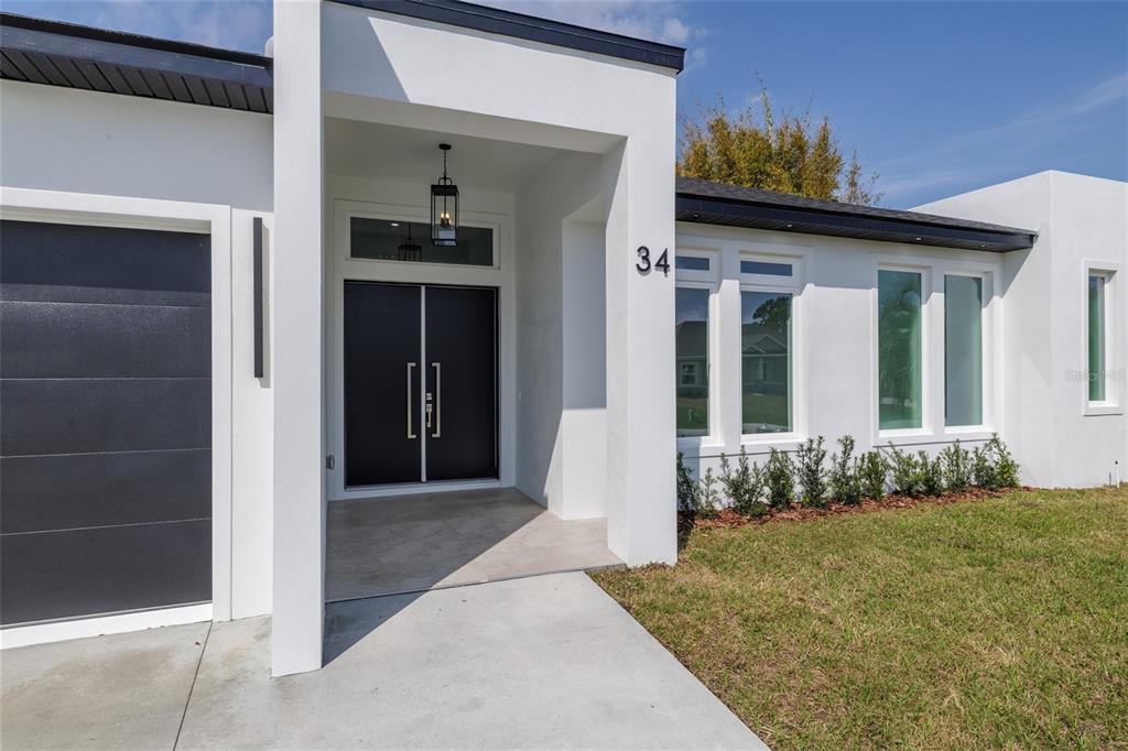 The exterior of a modern white house features a dark double door and garage door — 34 FALLEN OAK LANE, PALM COAST, FL