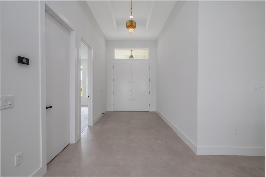 A bright entryway features white walls, tile flooring, a tray ceiling, and a gold chandelier — 34 FALLEN OAK LANE, PALM COAST, FL