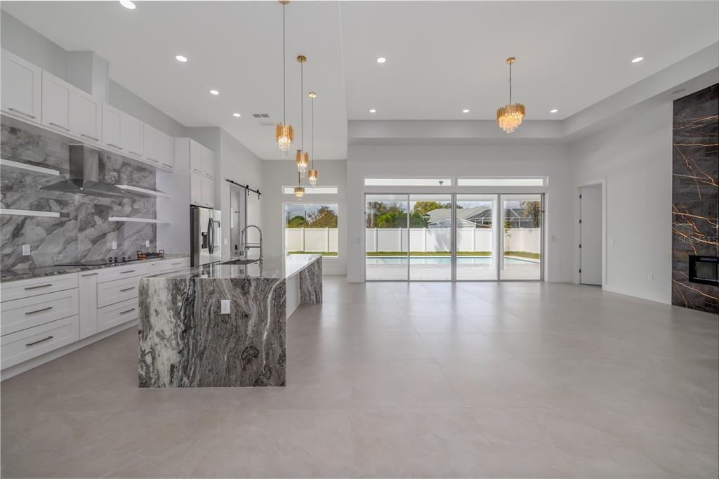 A modern open-concept kitchen and living area features marble countertops, white cabinetry, and sliding glass doors — 34 FALLEN OAK LANE, PALM COAST, FL