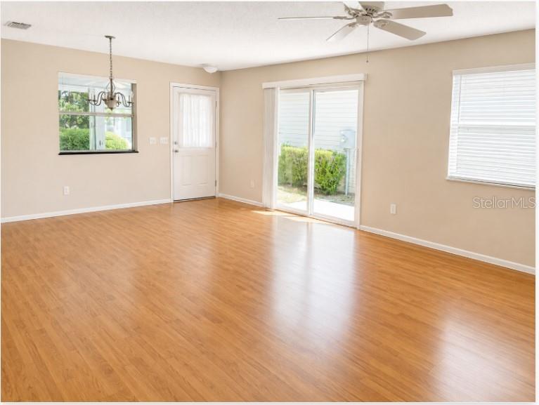 An empty room features light wood-look flooring, a ceiling fan, a chandelier, and sliding doors — 2340 PICKENS PLACE, THE VILLAGES, FL