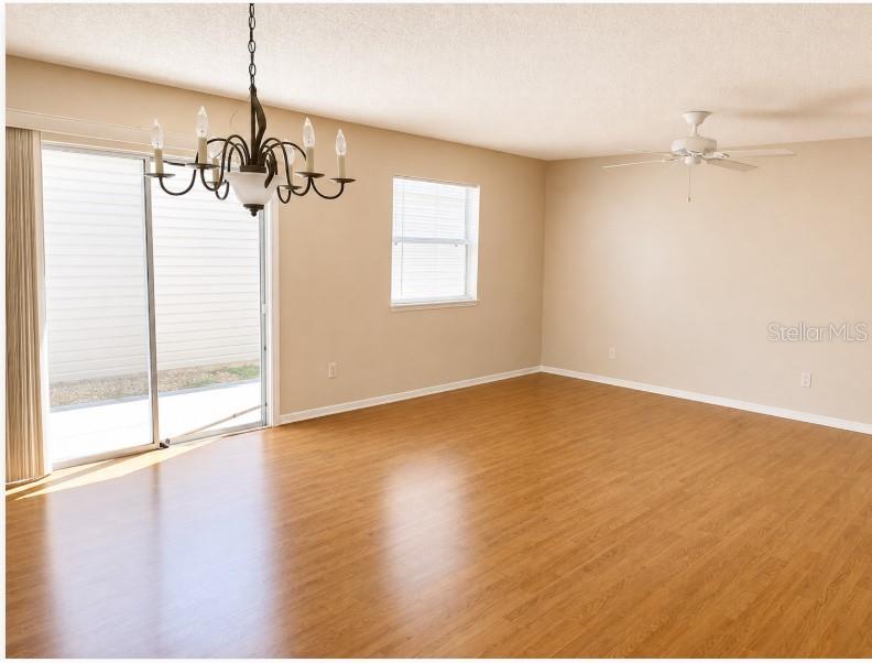 An empty living room features light wood-look flooring, a chandelier, a ceiling fan, and sliding doors — 2340 PICKENS PLACE, THE VILLAGES, FL