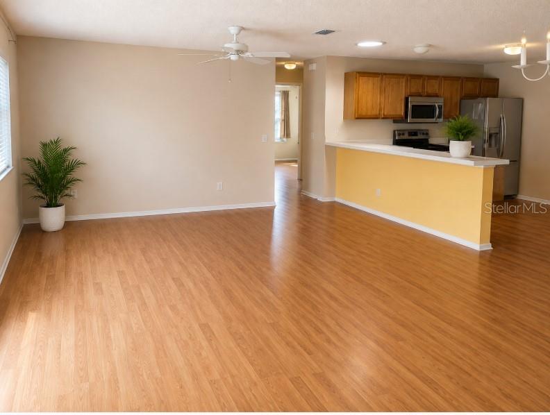 An open-concept living area features light wood flooring, a ceiling fan, and a kitchen with yellow walls — 2340 PICKENS PLACE, THE VILLAGES, FL