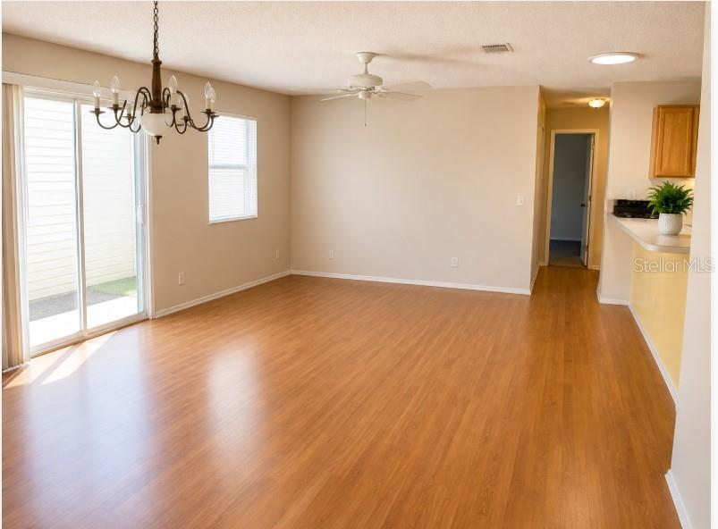 An empty living room features light wood-look flooring, a ceiling fan, and a sliding glass door — 2340 PICKENS PLACE, THE VILLAGES, FL