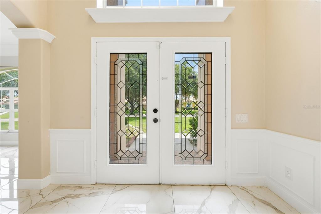 A bright entryway features white double doors with decorative glass panels and marble-look tile flooring — 11326 LEDGEMENT LANE, WINDERMERE, FL