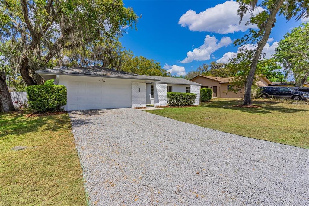 A single-story house with a white brick facade, a gravel driveway, and large oak trees — 437 ALPINE STREET, ALTAMONTE SPRINGS, FL