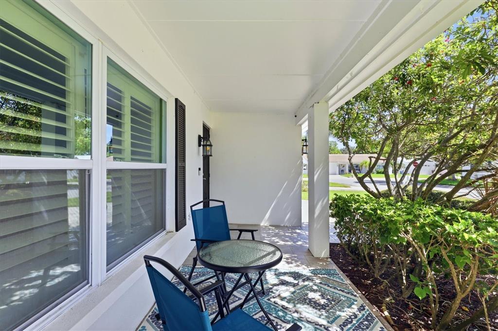 A covered front porch features a small glass table, two blue chairs, and a patterned rug — 9304 41ST STREET N, PINELLAS PARK, FL