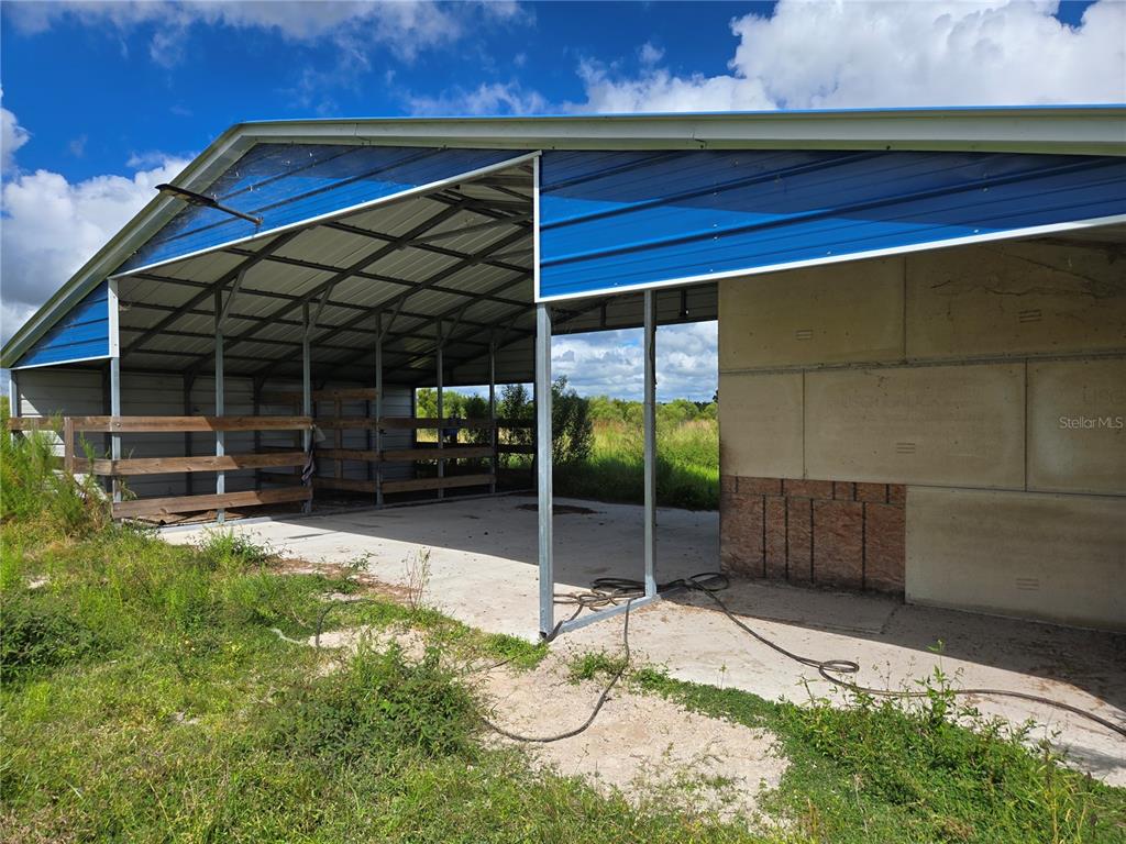 A partially enclosed metal barn structure with a concrete floor and wood stall dividers — SE PIGGY BACK ROAD, ARCADIA, FL