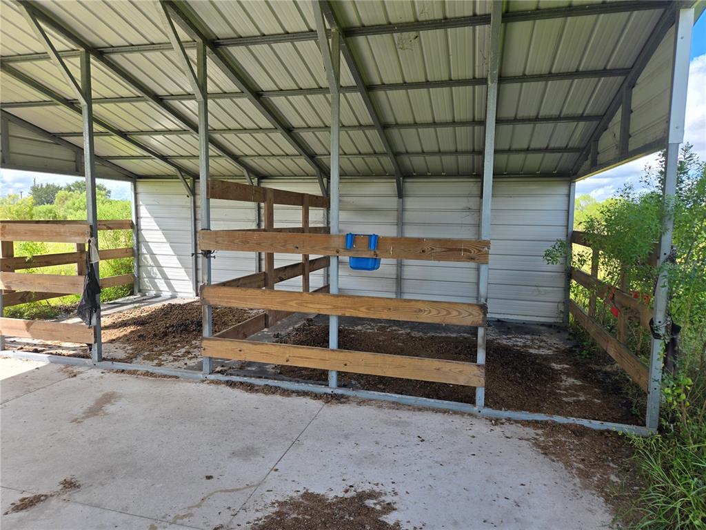 An open-sided metal barn structure features wooden stall partitions and a concrete floor — SE PIGGY BACK ROAD, ARCADIA, FL