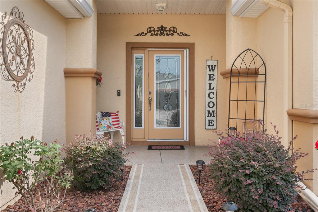 A front entryway features a tan door with glass panels, a welcome sign, and landscaping — 9215 SE 118TH LOOP, SUMMERFIELD, FL