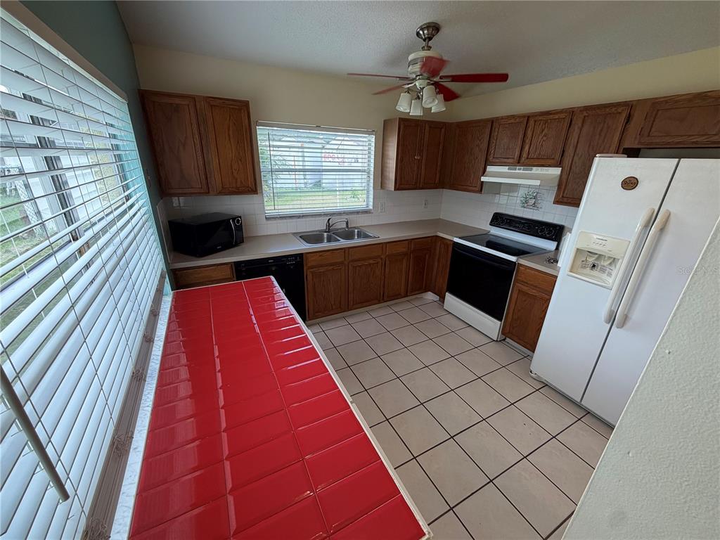 A kitchen features wood cabinets, white appliances, a red tiled counter, and beige floor tiles — 13015 BALTIMORE WOODS LANE, ORLANDO, FL