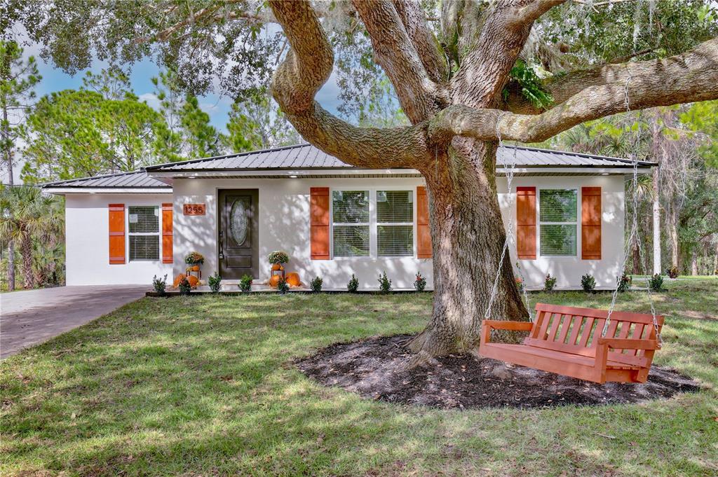 A single-story house with a metal roof, white stucco walls, and a large oak tree — 1255 FLINT TRAIL, GENEVA, FL