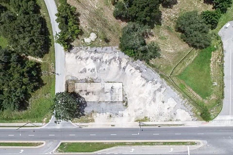 An aerial view shows a vacant lot with a concrete foundation slab and surrounding trees — E MYERS BOULEVARD, MASCOTTE, FL