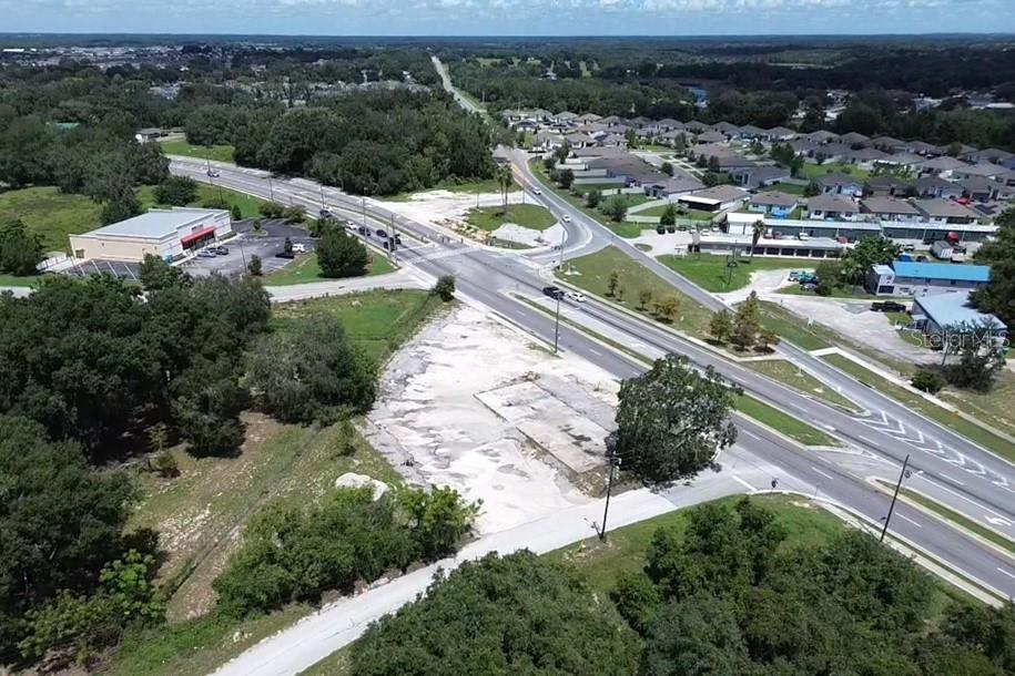 An aerial view shows a vacant lot adjacent to a road intersection and residential neighborhood — E MYERS BOULEVARD, MASCOTTE, FL