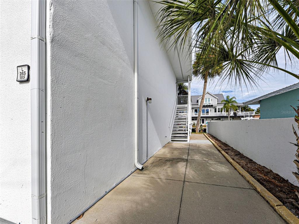 A concrete walkway runs between a white building wall and a low perimeter wall — 902 GIBBS ROAD UNIT 285, VENICE, FL