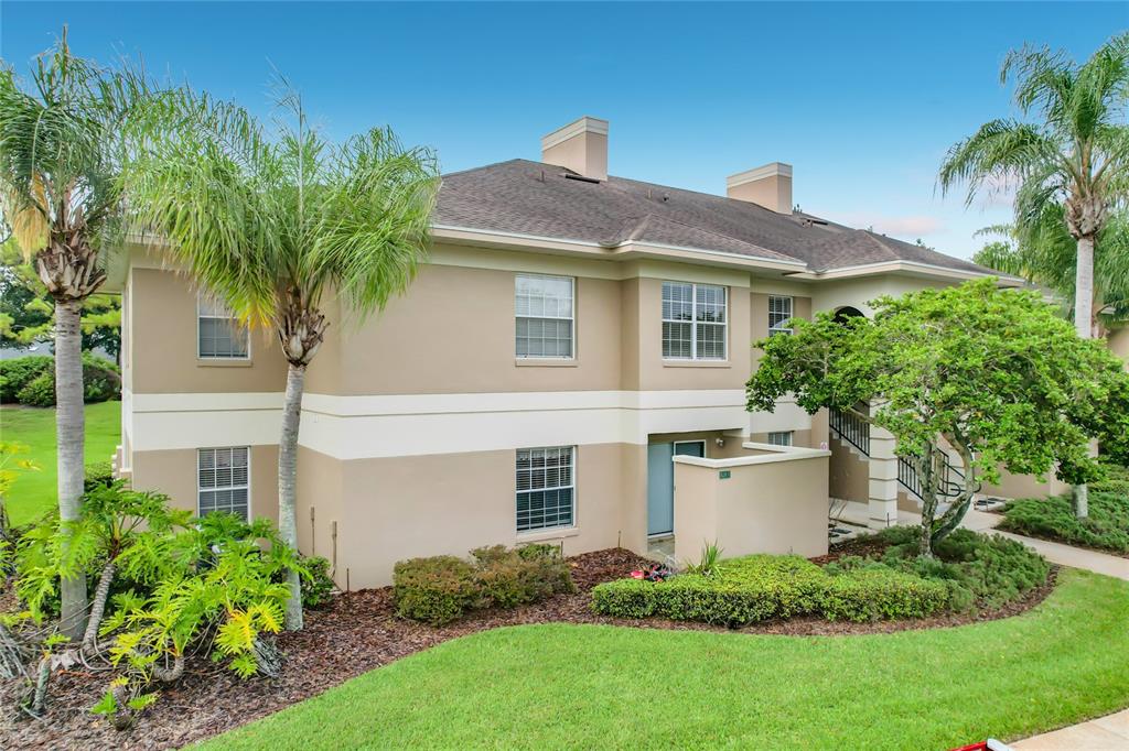 A two-story tan stucco apartment building features a shingled roof, palm trees, and landscaping — 1105 EAGLE POND DRIVE UNIT 1105, WINTER HAVEN, FL