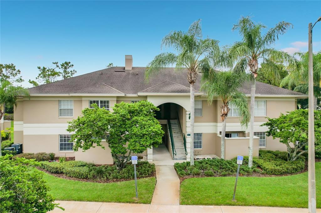 A two-story apartment building with a central staircase, palm trees, and a landscaped lawn — 1105 EAGLE POND DRIVE UNIT 1105, WINTER HAVEN, FL