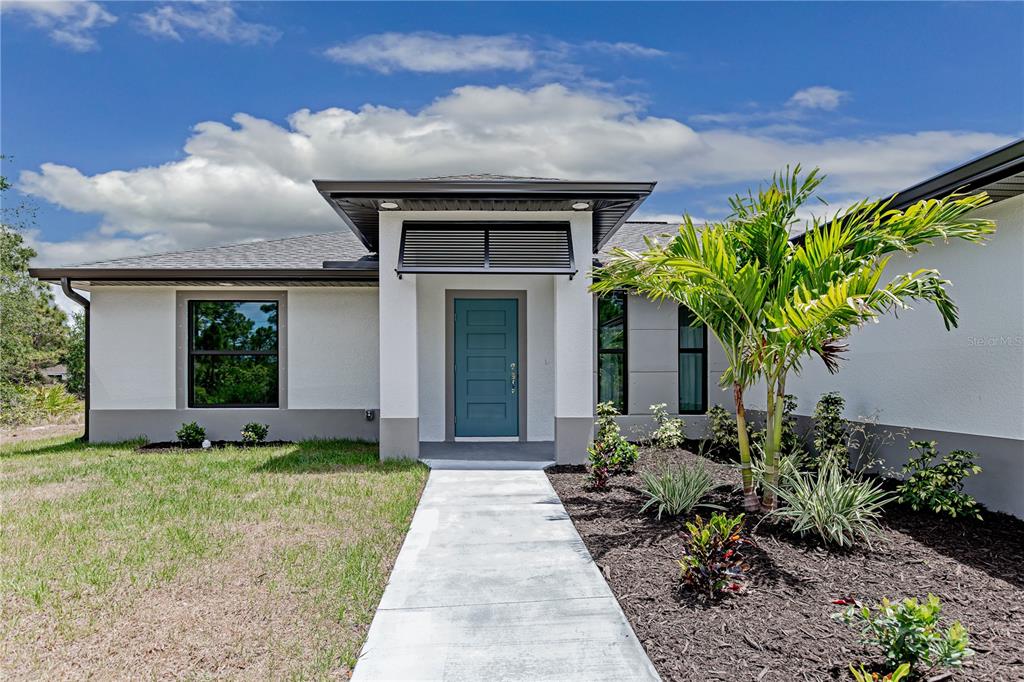 The exterior of a modern one-story house features a teal front door and landscaping — 13349 MENORAH DRIVE, PUNTA GORDA, FL