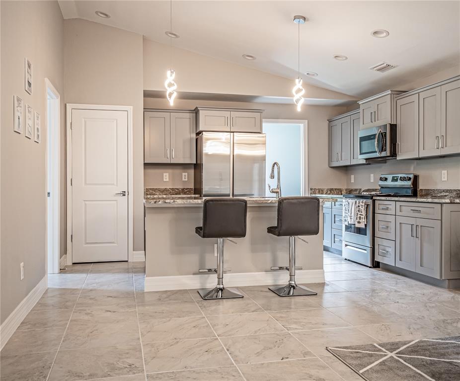 A kitchen features gray cabinets, stainless steel appliances, a breakfast bar, and tile flooring — 13349 MENORAH DRIVE, PUNTA GORDA, FL