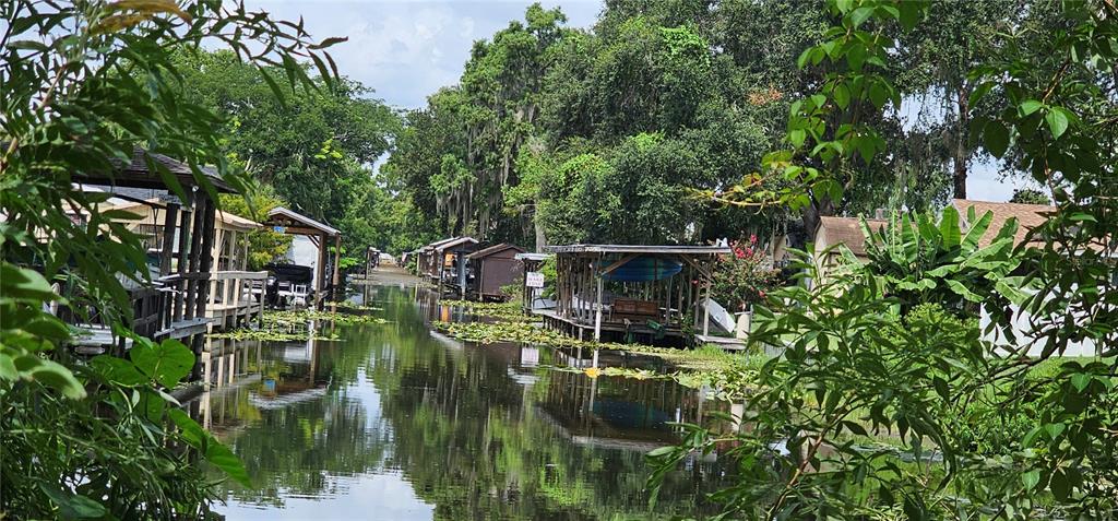 A canal lined with boat docks and lush trees leads toward houses in the distance — PINE ISLAND DRIVE, LEESBURG, FL