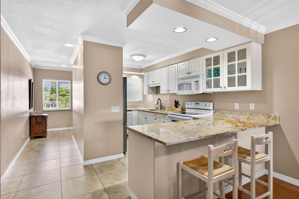 A kitchen with white cabinets, granite countertops, and a breakfast bar with two wooden stools — 1008 APOLLO BEACH BOULEVARD UNIT 206, APOLLO BEACH, FL