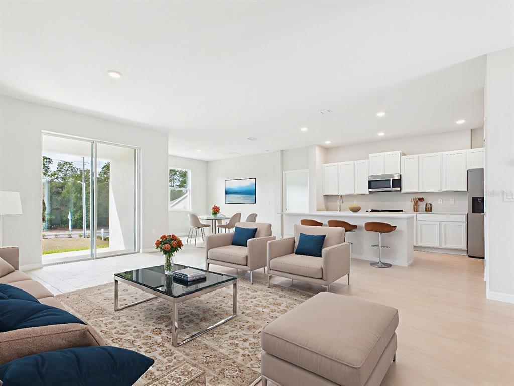 A bright, open-concept living room and kitchen area features white cabinetry and neutral furniture — 8419 N INCA WAY, DUNNELLON, FL