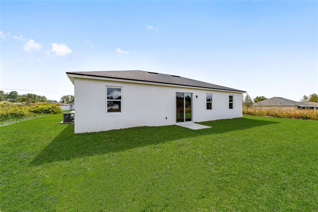 The rear exterior of a white, single-story house features a sliding glass door and windows — 8419 N INCA WAY, DUNNELLON, FL