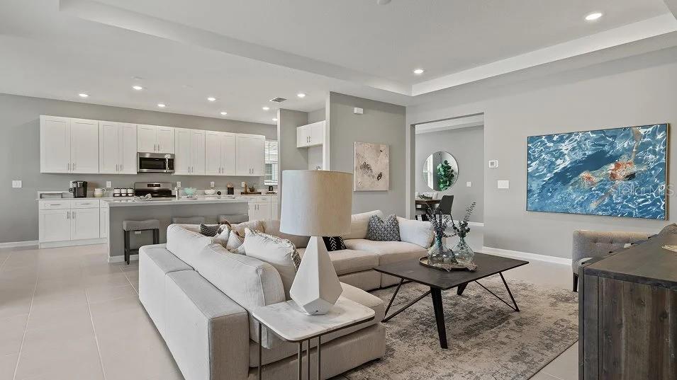 An open-concept living room with a sectional sofa, coffee table, and adjacent kitchen with island — 1801 RIDER RAIN LANE, APOPKA, FL