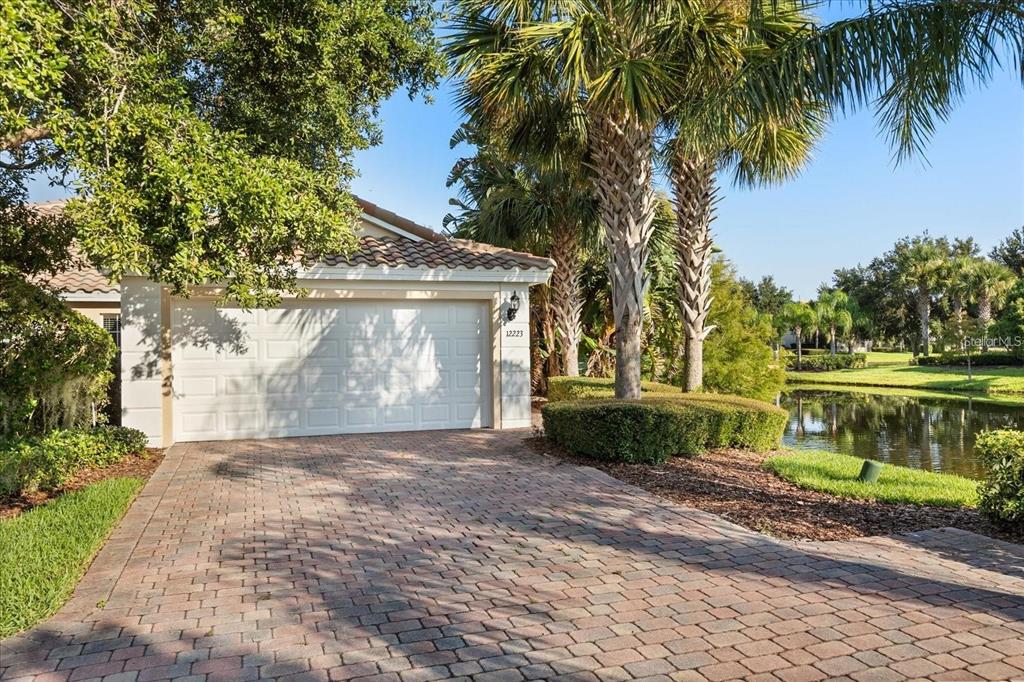 A paved driveway leads to a white garage door next to a pond and palm trees — 12223 PESCARA LANE, ORLANDO, FL