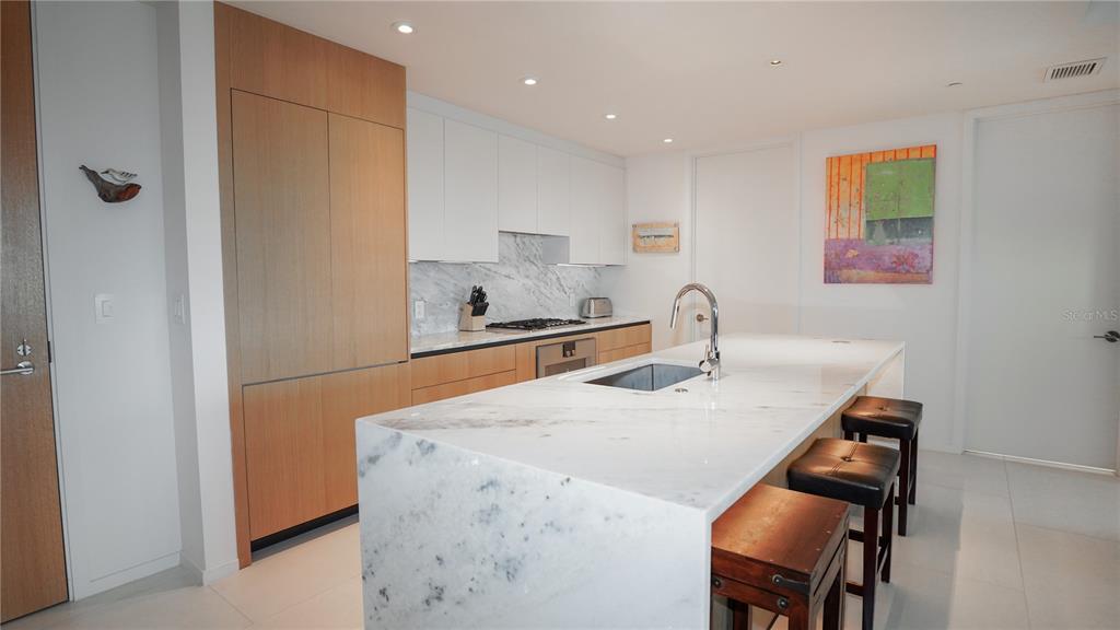 A modern kitchen features a marble waterfall island, light wood cabinetry, and white upper cabinets — 1020 SUNSET POINT ROAD UNIT 512, CLEARWATER, FL