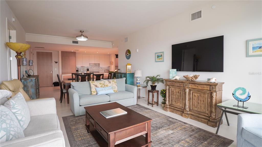 A living room with a sofa, coffee table, and television mounted above a wooden cabinet — 1020 SUNSET POINT ROAD UNIT 512, CLEARWATER, FL