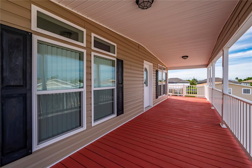 A long, covered porch with red wooden decking, white railings, and tan vinyl siding — 67 WINDMILL BOULEVARD, PUNTA GORDA, FL