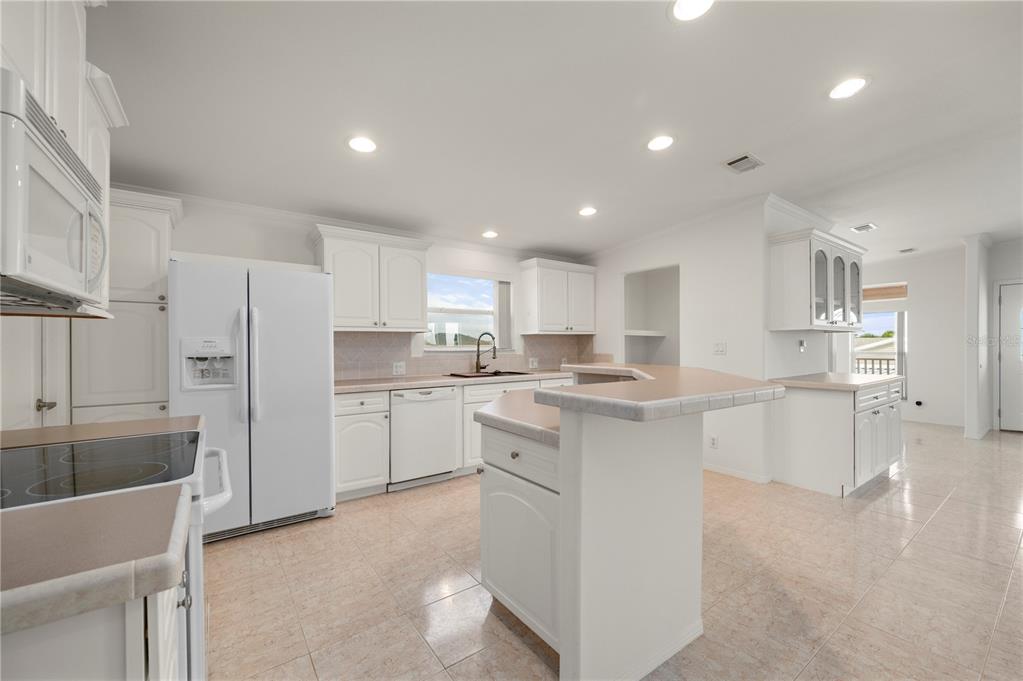 A white kitchen features a central island, light-colored countertops, and tile flooring — 67 WINDMILL BOULEVARD, PUNTA GORDA, FL