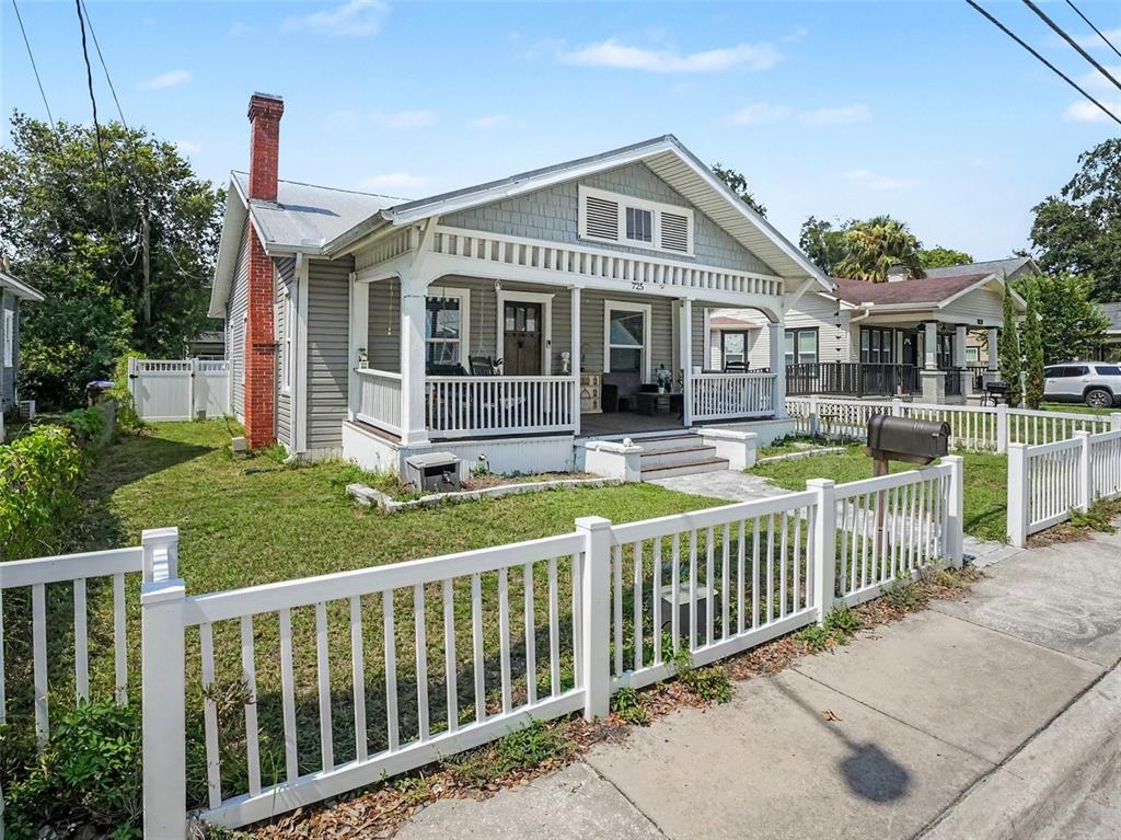 A single-story house with a front porch, white picket fence, and brick chimney at dusk — 725 MABBETTE STREET, KISSIMMEE, FL