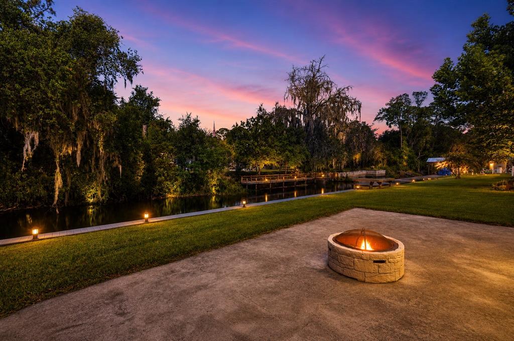 A fire pit sits on a concrete patio overlooking a grassy lawn and a canal — 1330 S SHORE DRIVE, ST CLOUD, FL