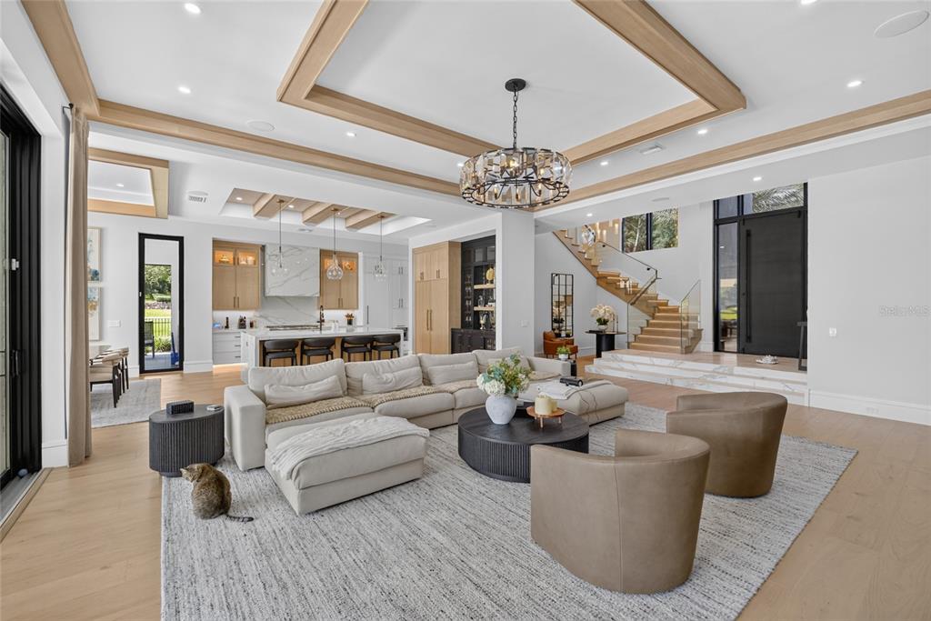 A spacious open-concept living room features a large sectional, modern chandelier, and a floating staircase — TBD SE 12 CIRCLE, OCALA, FL