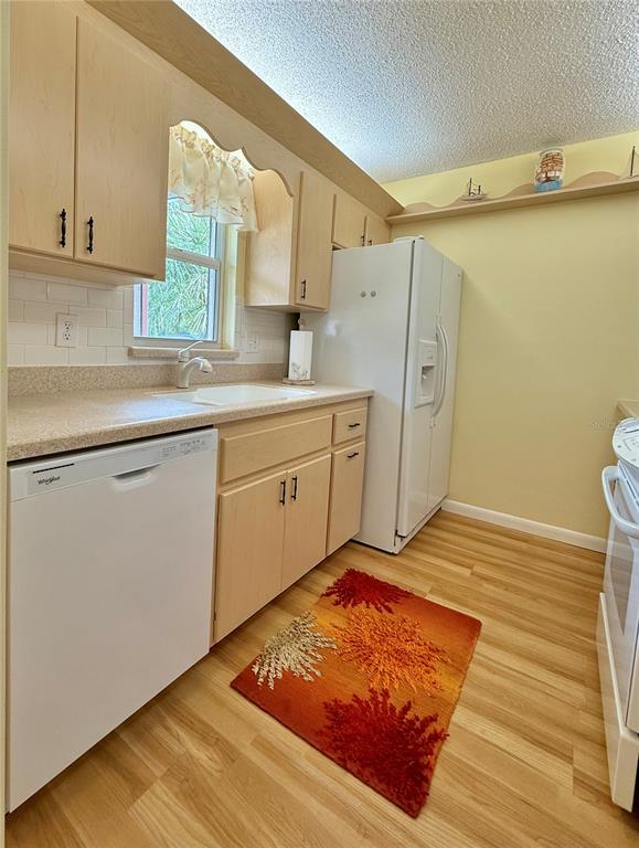 A kitchen features light wood cabinets, white appliances, a white subway tile backsplash, and wood flooring — 4827 CADAGUA DRIVE, SEBRING, FL