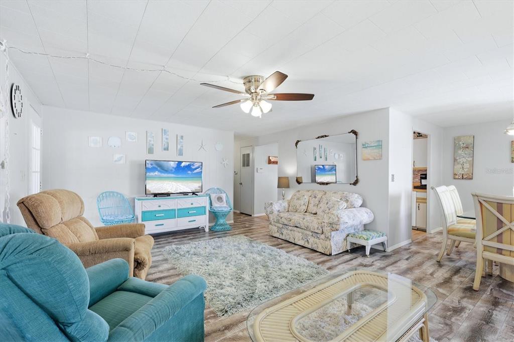 A living room features a floral sofa, a teal armchair, and a television on a dresser — 1003 44TH AVENUE DRIVE E, ELLENTON, FL