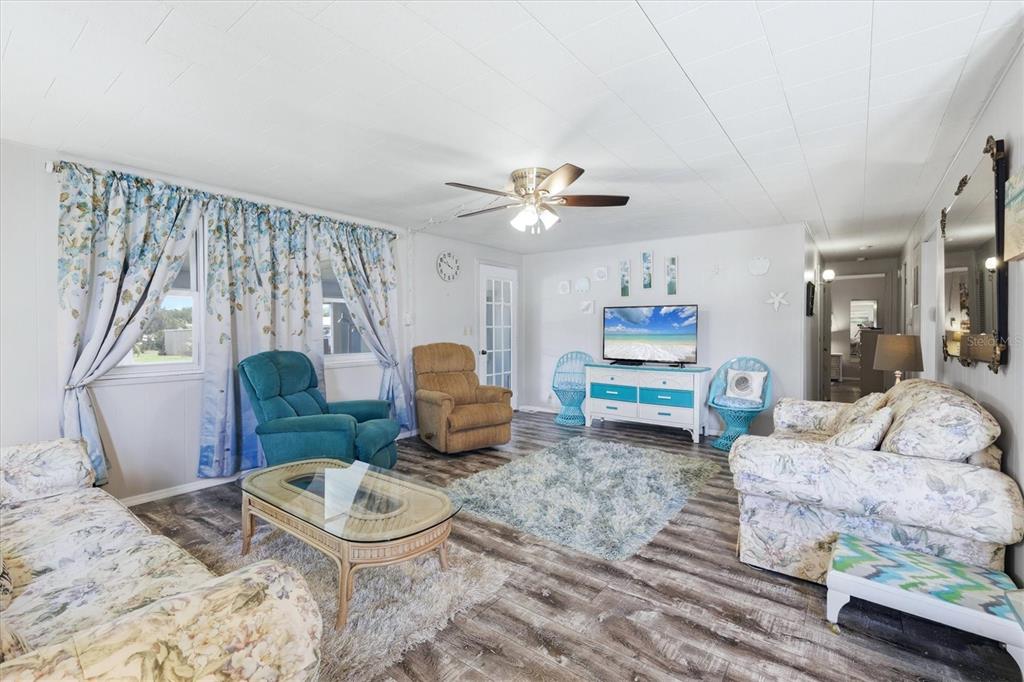 A living room features wood-look flooring, floral sofas, a blue recliner, and a television console — 1003 44TH AVENUE DRIVE E, ELLENTON, FL