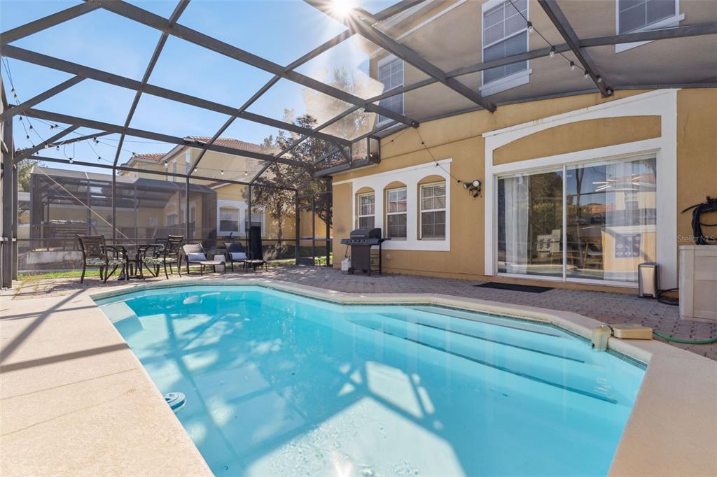 A swimming pool sits on a paved patio enclosed by a screened lanai behind a house — 8572 BAY LILLY LOOP, KISSIMMEE, FL