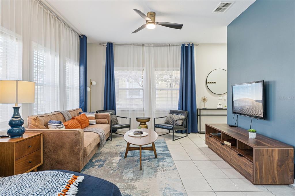 A living room features a brown sofa, two black chairs, a television, and blue curtains — 8572 BAY LILLY LOOP, KISSIMMEE, FL