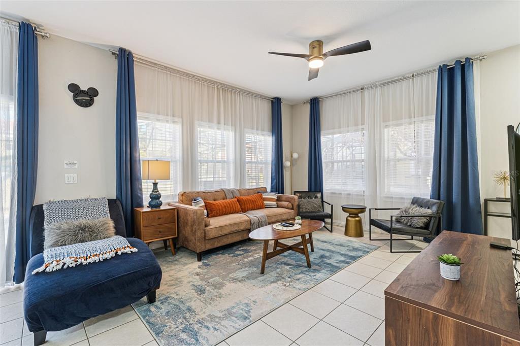 A living room features a brown sofa, blue chaise, area rug, and floor-to-ceiling curtains — 8572 BAY LILLY LOOP, KISSIMMEE, FL