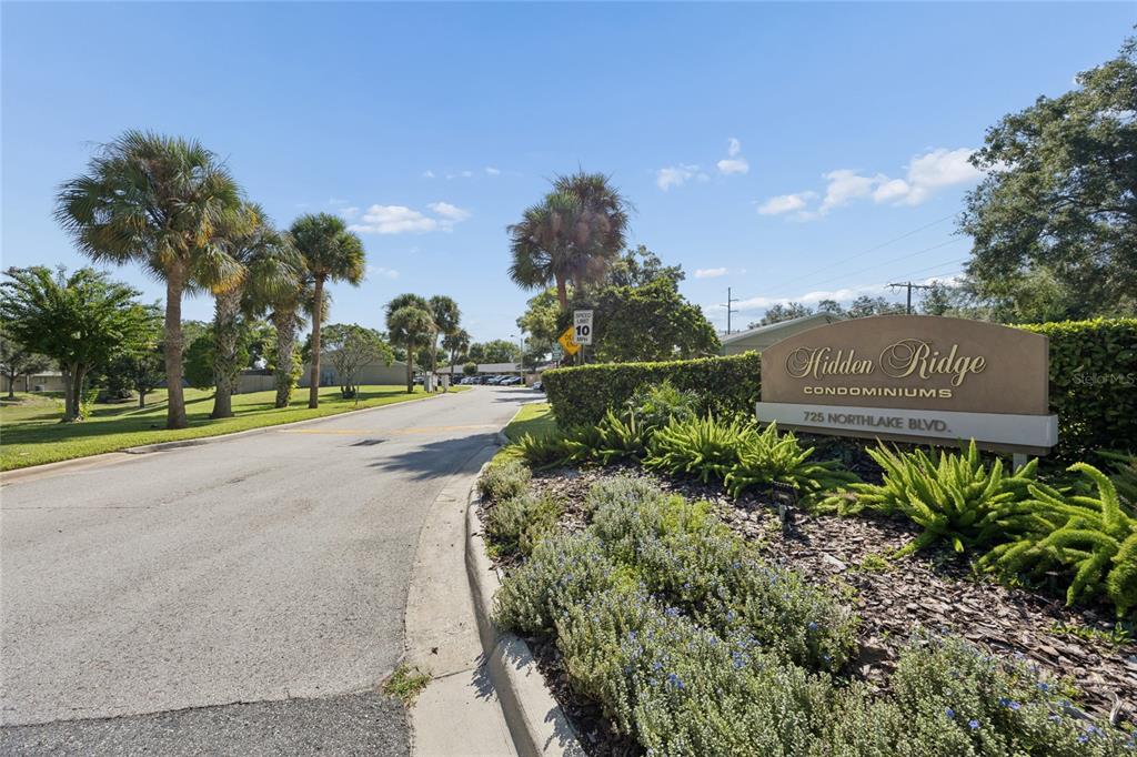 The entrance to Hidden Ridge Condominiums features a sign, palm trees, and a paved road — 725 NORTHLAKE BOULEVARD UNIT 10, ALTAMONTE SPRINGS, FL