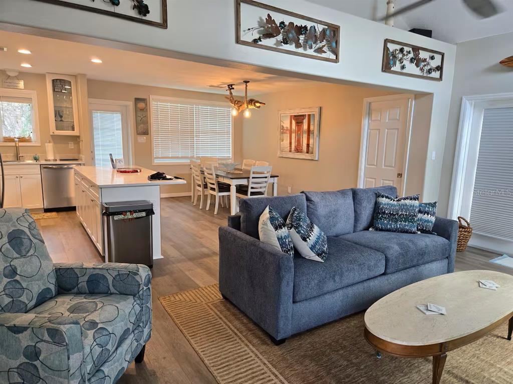An open-concept living room and kitchen featuring a blue sofa, dining area, and white cabinetry — 117 79TH STREET, HOLMES BEACH, FL