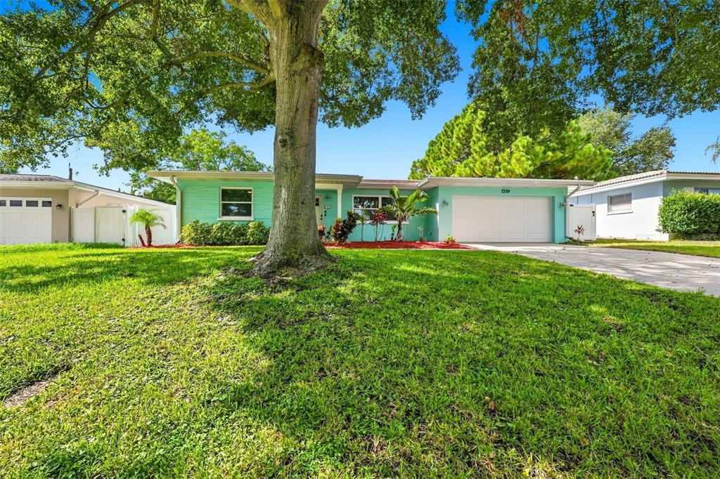 A single-story, light green house with a two-car garage and a large tree in front — 1359 HOWARD STREET, CLEARWATER, FL