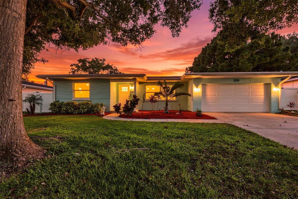 A single-story house with a light green exterior, white garage door, and a sunset sky — 1359 HOWARD STREET, CLEARWATER, FL