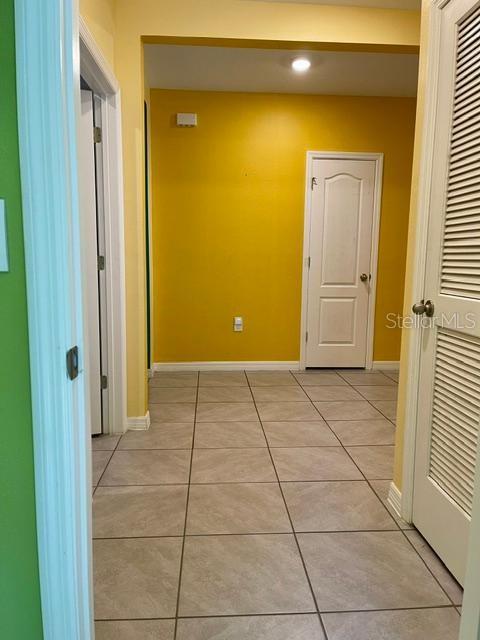 A hallway with light-colored tile flooring leads to a yellow wall and a white door — 1810 EAGLE HAMMOCK BOULEVARD, EAGLE LAKE, FL