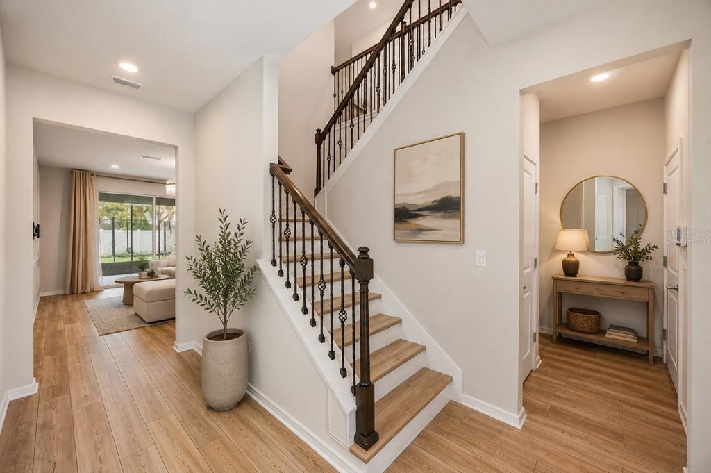 A bright entryway features a wooden staircase with iron railings, light wood flooring, and decor — 2993 PIER POINTE LANE, CLEARWATER, FL